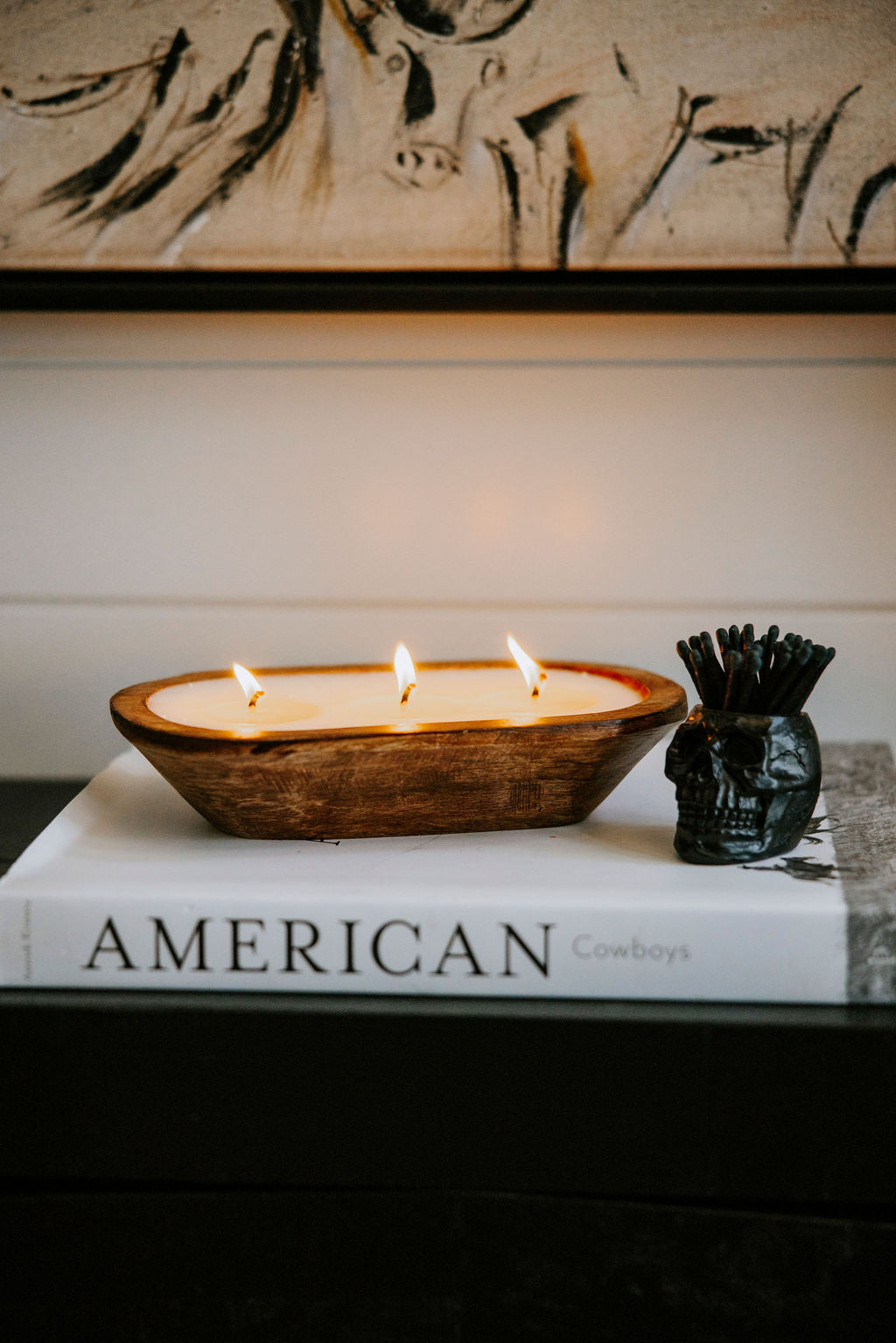 A lit three-wick dough bowl candle on top of a book, with a matchstick holder in the shape of a skull